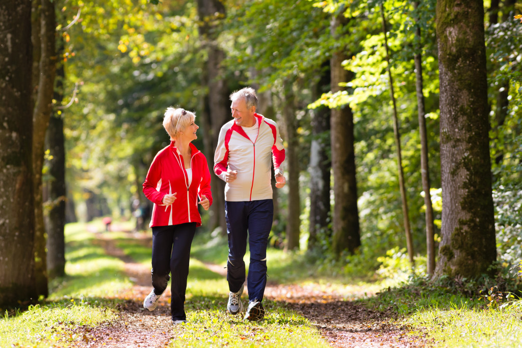 Senior Couple doing sport outdoors, jogging on a forest road in the autumn
