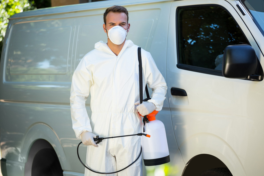 Man holding equipment and spray for pest control in front of white van