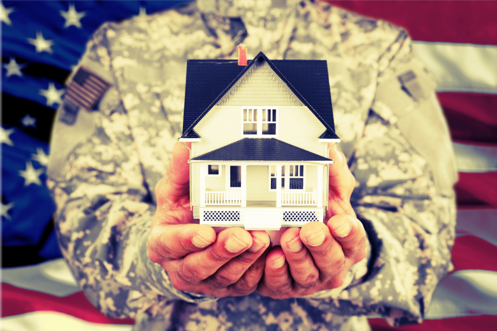 A soldier holding a miniature house in front of the US flag