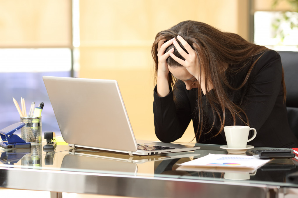 A woman is holding her head in front of a laptop in an office